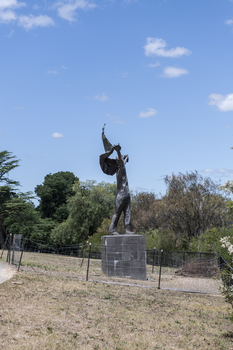 A statue of a naked man waving a piece of cloth throwing his hands up in the air. The whole statue including the cloth is cast in bronze.
