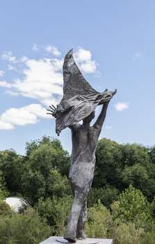 A statue of a naked man waving a piece of cloth throwing his hands up in the air. The whole statue including the cloth is cast in bronze.