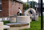 A large abstracted sculpture made out of stone that resembles a play structure structure or outdoor seating. it is in a grassy part out the front of a community hub. 