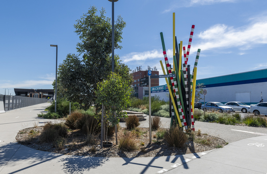 A large sculpture consisting of a series of striped and unstriped metal poles sticking out of the ground in a single cluster in a haphazard manner. there are approximately 15 of them and the sculpture is located on a street corner.