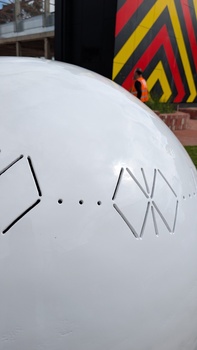 A detailed picture of  a large metal sphere sculpture with abstract butterfly motifs cut into it.