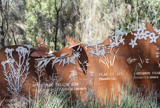 A large rusted cut out sculpture with native floral emblems form the local area. it is located in a bush setting along a creek.