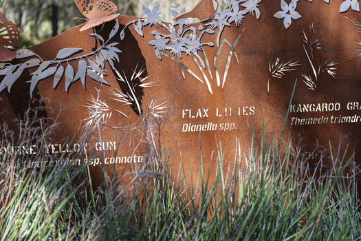 A large rusted cut out sculpture with native floral emblems form the local area. it is located in a bush setting along a creek.