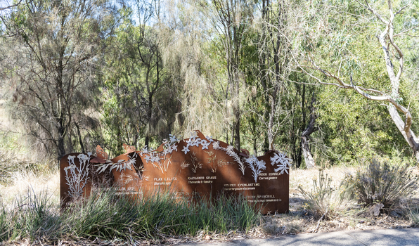A large rusted cut out sculpture with native floral emblems form the local area. it is located in a bush setting along a creek.