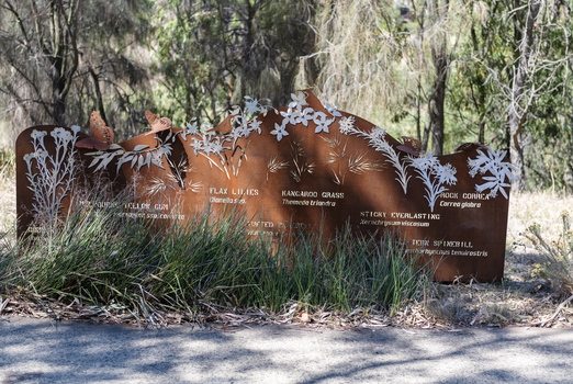 A large rusted cut out sculpture with native floral emblems form the local area. it is located in a bush setting along a creek.