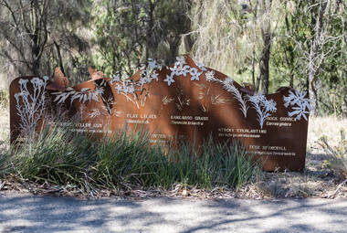 A large rusted cut out sculpture with native floral emblems form the local area. it is located in a bush setting along a creek.