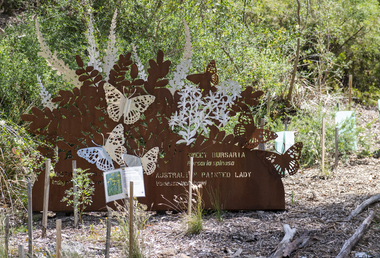 A large rusted cut out sculpture with native floral and emblems form the local area. It also includes 3 silver butterfly's. It is located in a bush setting along a creek.