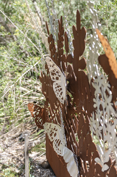 A large rusted cut out sculpture with native floral and emblems form the local area. It also includes 3 silver butterfly's. It is located in a bush setting along a creek.