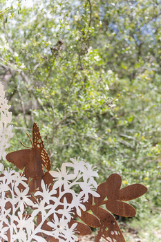 A large rusted cut out sculpture with native floral and emblems form the local area. It also includes 3 silver butterfly's. It is located in a bush setting along a creek.