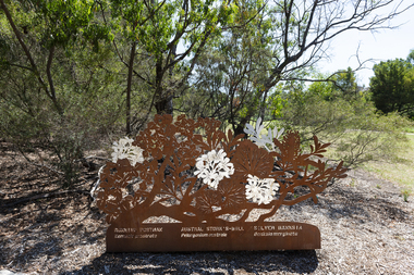 A large rusted cut out sculpture with native floral emblems form the local area. it is located in a bush setting along a creek.