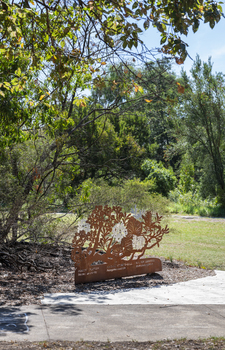 A large rusted cut out sculpture with native floral emblems form the local area. it is located in a bush setting along a creek.