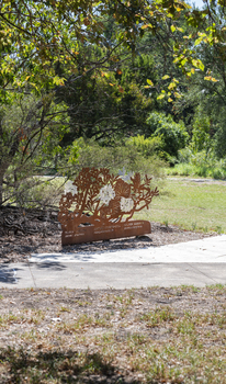 A large rusted cut out sculpture with native floral emblems form the local area. it is located in a bush setting along a creek.