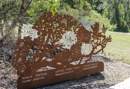 A large rusted cut out sculpture with native floral emblems form the local area. it is located in a bush setting along a creek.