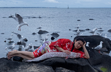 Woman in red dress lying on a stony beach with hand on large fish