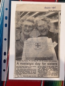 Two elderly women smiling and holding a novelty cake shaped like a house. The newspaper clipping is titled 'A nostalgic day for sisters'