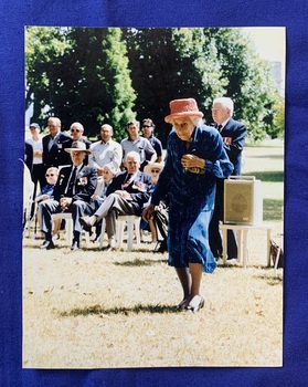 Colour photograph of Cate Hewins at the Australian Hospital Ship (AHS) Centaur Memorial dedication event on the 21st of January 2001. Cate is wearing a pink crocheted hat with a blue suit and skirt ensemble adorned with medals, with others seated and standing in the background. 