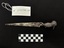 Photo of silver, chrome-plated letter knife, with kookaburra hilted handle, upon black fabric. On one of the blade faces the logo of the Adelaide Steamship Company, a white flag, with a blue cross and an eight-pointed red star in the centre. On the blade face accompanying the flag the ship name, M.V. Manunda, is also pressed into the blade. On the opposing face of the blade, a makers mark and silver quality mark is present. Scale card and object number also present. 