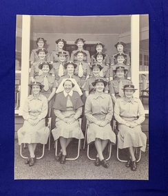 A black and white photograph of 18 women wearing their uniforms and sitting in four tiered rows, 17 nurses and 1 matron.