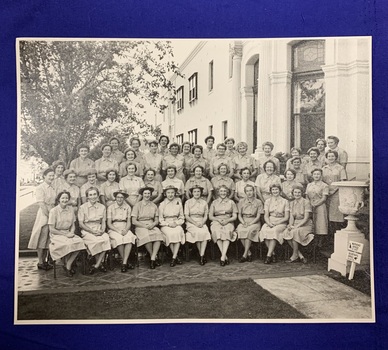 A black and white photo of 45 women in uniform in 4 tiered rows outside a large building.