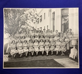 A black and white photo of 45 women in uniform in 4 tiered rows outside a large building.