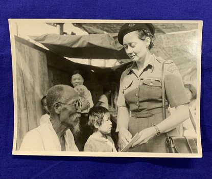 A black and white photograph of P M McCarthy in uniform [presumably in Korea] pointing to a piece of paper or card, whilst an older [Korean] man reads it. There are children and a girl with a fan smiling in the background. 