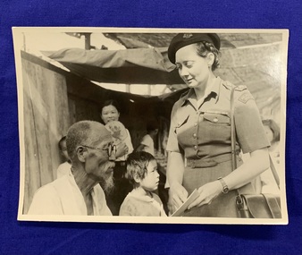 A black and white photograph of P M McCarthy in uniform [presumably in Korea] pointing to a piece of paper or card, whilst an older [Korean] man reads it. There are children and a girl with a fan smiling in the background. 
