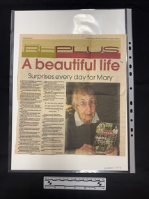 Newspaper clipping with colour heading and photo of an elderly woman holding a book titled 'Caped crusaders' with two columns of text.