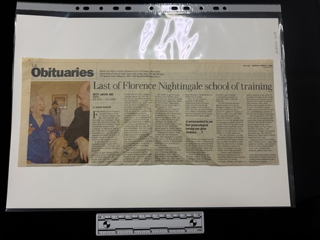Newspaper clipping with a colour photograph on the left hand side of an older man and woman in the foreground and an older woman in the background.  The obituary has six columns of text.