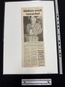 Newspaper clipping with a headline and large black and white photograph of a elderly woman holding an award in her lap.  The article has three columns of text.