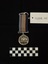Photo of the obverse of a Australia Service Medal. Made from nickel-silver, the obverse has a central and textured design of the Australian coat of arms. The face has 'THE AUSTRALIA SERVICE MEDAL/1939-1945' inscribed. The rim of the medal has two engravings: 'VFX53656/J.G. GIBSON'. The ribbon is tactile, feeling ribbed under finger. This photograph is taken upon a black background, with a scale card and object number included.