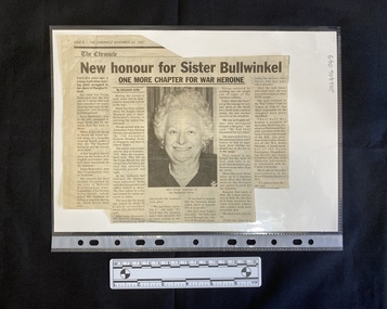 A newspaper clipping with six columns of text and a centred black and white photo of an older woman