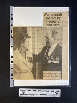 A newspaper clipping of a large black and white photo of a woman and a man with a title and caption