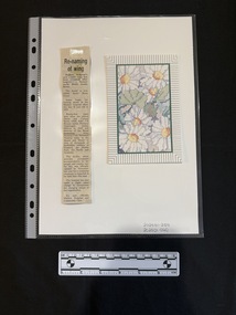A card with a picture of colorful flowers, framed by stripes, sitting to the right of a newspaper clipping with a headline and single column of text