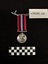 Back view of the War Medal 1939-1945. The silver coloured medal has a lion standing on a double-headed dragon. The ribbon is coloured in vertical strips: red, blue, white, red, white, blue, red, it is tactile, feeling ribbed under finger. This photograph is taken upon a black background, with a scale card and object number included.