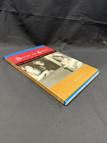 Paperback book with spine and cover in blue, mustard yellow and brick red.  Cover also has a black and white photograph of a nurse holding an infant with a nurse and man looking on through a window.