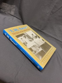Hardback book with olive green, blue, red and white cover and writing.  Cover has sepia image of two nurses working in a hospital ward, one talking to a patient in a bed.