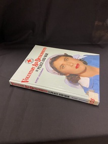 Hardcover book with a light green cover. The Title is printed in red and black. There is a female nurse on the front cover in a blue uniform and white red cross head scarf. The Australian Red Cross symbol is at the top of the front cover.