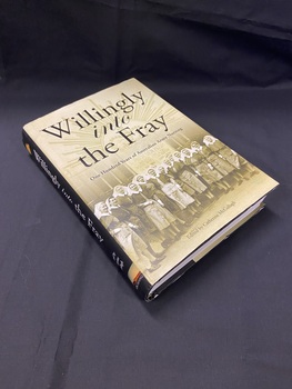 Black hardcover book with dustjacket. Dustjacket has a black spine with white writing. Front cover of dust jacket is a sepia tone image of 14 female nurses in uniform standing in front of the Australian General Hospital in 1942.