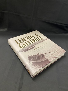 Hardcover book with dust jacket. Lettering is in gold print and there is a sepia toned image that wraps around the cover depicting the first party of officers landing on Lemnos Island in 1915.