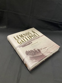 Hardcover book with dust jacket. Lettering is in gold print and there is a sepia toned image that wraps around the cover depicting the first party of officers landing on Lemnos Island in 1915.