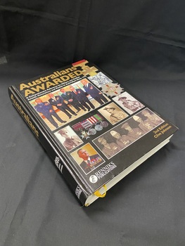 Hardcover book with Australian Awarded printed at the top in gold letters. Below the title are seven photos of differing sizes set out in rows, they show a range of different men in various uniforms that have been awarded medals. Five of the photos are black and white images of men in military uniforms and the other two are coloured photos of civilian men wearing an assortment of medals. There is an image of four medals displayed together in the centre of the cover, and an ornate medal is shown on the right hand side . At the top right corner there is a gold medal of valour.