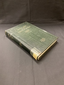 Dark green hardback book. 'Who's who in the world of women' is printed at the top of the cover in faded yellow print, in the lower centre of the cover are the words 'Victoria Australia 1930' they have faded and blurred with time. There is a sticker on the bottom of the spine with an old cataloguing number attached with a  piece of yellowing tape.