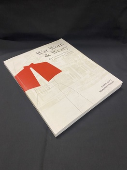 Paperback book with a white cover showing a basic outline of a nurse wearing a red cape. The title and author details are printed in black and in the background is a faded photo of a hospital building.