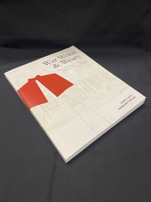 Paperback book with a white cover showing a basic outline of a nurse wearing a red cape. The title and author details are printed in black and in the background is a faded photo of a hospital building.
