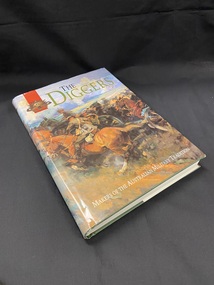 Hardcover book with dustjacket. 'THE DIGGERS' is printed at the top in olive green letters and just to the right is the Australian Commonwealth Military Forces emblem on a red panel. The cover shows a painting of soldiers on horseback charging across a field. At the bottom of the cover is printed in white text : makers of the Australian Military tradition.