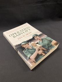 White book with a picture of two women in green uniforms, one of whom is holding a baby, in front of a building with a corrugated roof. The title 'OPERATION BABYLIFT' is printed above the image in green, followed by the author's name in red text. At the top of the page it reads "The incredible story of the inspiring Australian women who rescued hundreds of orphans at the end of the Vietnam War".