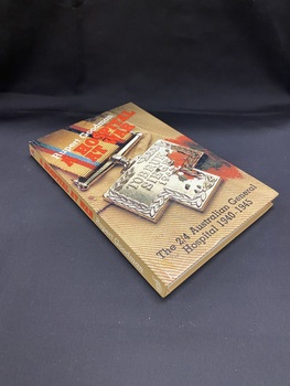 Light brown cover and spine. The title is printed diagonally near the top of the cover in red print, with the author's name above that in white print. At the bottom of the cover is the sub-title in black print. The background of the entire cover is a close-up image of the fabric of a soldier's uniform with a bullet wound and a silver medallion that reads 'Tobruk siege 1941'.