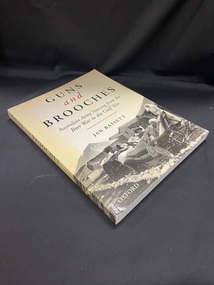 Cream coloured softcover book that has yellowed around the borders. The title is printed in black and red text across the top half of the cover, the lower half shows a photographic image of patients lying on stretchers covered in blankets and being tended to by nursing staff outside field hospital tents. The image is black and white.