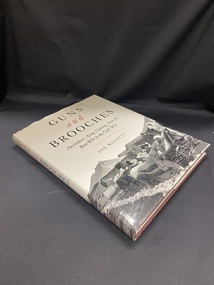 Maroon coloured hardcover book covered with a grey dustjacket. The title is printed in black and red text across the top half of the cover, the lower half shows a photographic image of patients lying on stretchers covered in blankets and being tended to by nursing staff outside field hospital tents. The image is black and white.