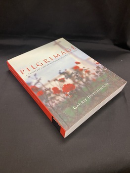 Cover has a red spine with white and balck text. The front cover shows red rose bushes with a faded building in the background. The title is printed towards the top of the page in red print, with the sub-title just below it in black. At the bottom of the cover is the author's name printed in white.